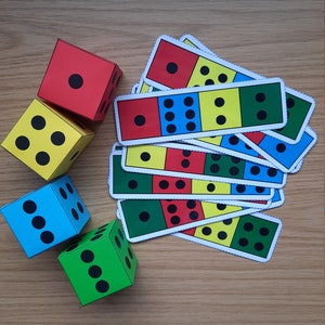May include: Four colourful dice with black dots and a stack of matching cards with red, yellow, blue, and green sections with black dots. The cards are for a dice game.