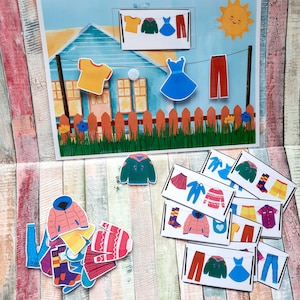 Peut inclure: Un ensemble coloré de vêtements en feutre pour un jeu de correspondance pour enfants. Les pièces comprennent une variété de vêtements tels que des chemises, des pantalons, des robes, des pulls et des chaussettes. Les pièces sont disposées sur un fond en bois avec un motif rayé bleu et blanc.