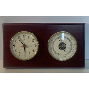 May include: A mahogany wood framed clock and barometer set with gold trim. The clock face has black hands and black Roman numeral markings. The barometer has a white face with black markings and a gold needle.