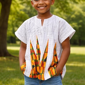 Puede incluir: Una camisa blanca de manga corta con cuello en V y patrones geométricos coloridos. La camisa se combina con vaqueros azules. El diseño de la camisa incorpora acentos naranjas, amarillos, verdes y negros.