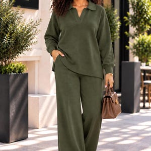 Peut inclure: Un ensemble deux pièces vert olive composé d'un haut à manches longues avec col et décolleté en V, assorti à un pantalon large. La tenue est complétée par des baskets blanches et un sac à main en cuir marron structuré avec des détails dorés.