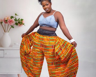 Könnte beinhalten: Eine Person trägt ein Jeans-Crop-Top und eine Hose mit leuchtend orangefarbenem, gelbem und grünem Muster. Die Hose hat ein weites, fließendes Design und einen schwarzen Bund. Weiße Turnschuhe vervollständigen das Outfit.