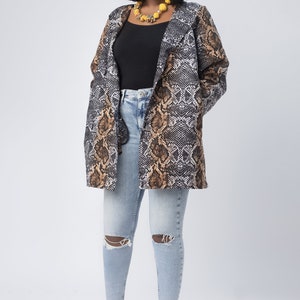 Może przedstawiać: Kobieta w czarnym, brązowym i beżowym żakiecie z nadrukiem wężowej skóry, na czarnym topie i jasnoniebieskich podartych dżinsach. Ma również na sobie żółty naszyjnik z koralików i złote szpilki. Żakiet jest głównym elementem.