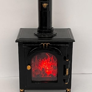 May include: Miniature black stove with a chimney and a glowing red fire effect inside. The stove has gold-colored accents on the door, legs, and chimney. The stove is a decorative item.