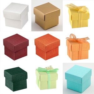 Könnte beinhalten: Eine Sammlung quadratischer Geschenkboxen in verschiedenen Farben: Weiß, Gold, Rot, Orange, Grün, Hellgrün und Blau. Einige Boxen sind schlicht, andere mit Bändern verziert. Die Boxen haben eine strukturierte Oberfläche, ca. 7.5 cm x 7.5 cm.