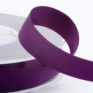 May include: A spool of deep purple ribbon with a satin finish. The ribbon is partially unrolled, showing a smooth, textured surface. The ribbon is suitable for crafts, gift wrapping, or decorative use.