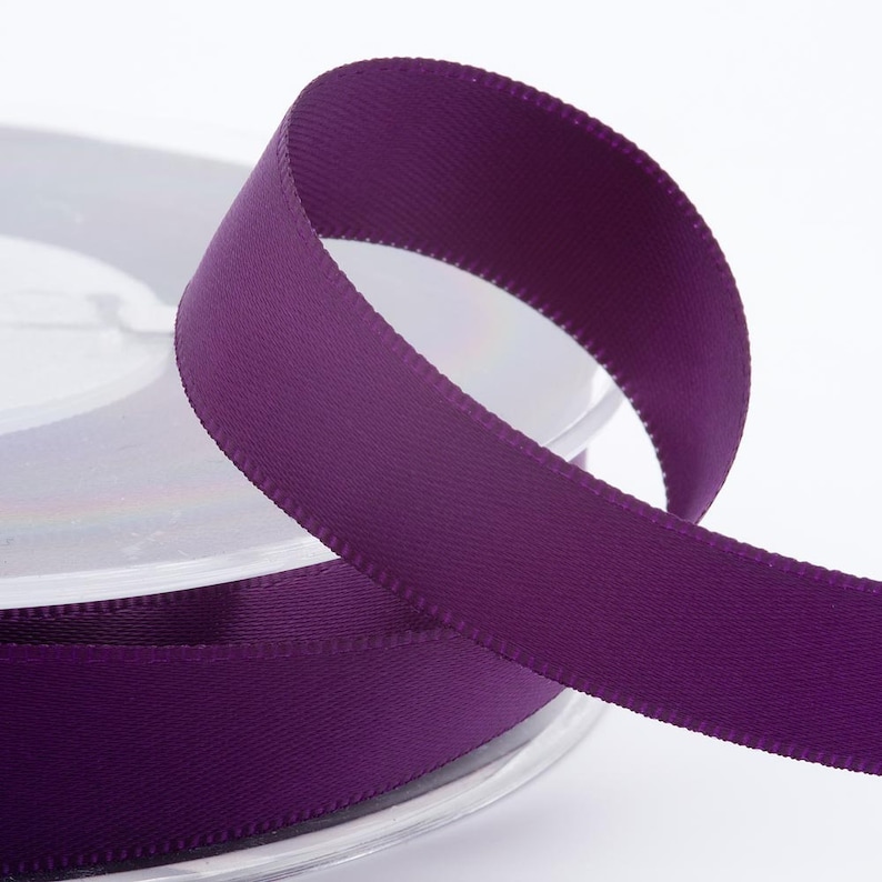 May include: A spool of deep purple ribbon with a satin finish. The ribbon is partially unrolled, showing a smooth, textured surface. The ribbon is suitable for crafts, gift wrapping, or decorative use.
