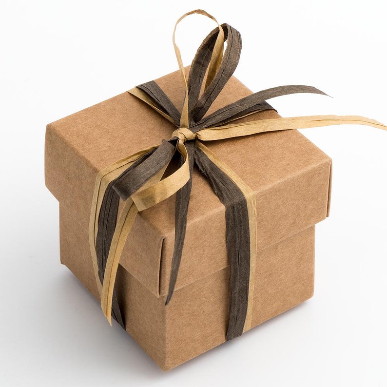 Op de afbeelding: Een kleine, bruine kartonnen geschenkdoos met een zwart en gouden lint dat in een strik is gebonden.
