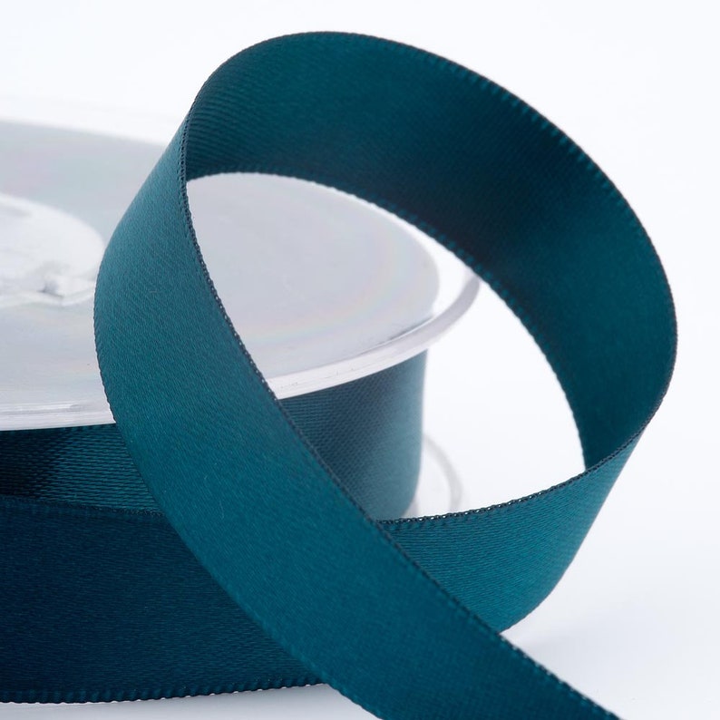 May include: A spool of teal ribbon with a textured surface. The ribbon is unwound, forming a loop, showing its smooth, finished edges. The ribbon is suitable for crafts, gift wrapping, or decorative use. The ribbon is approximately 1.27 cm wide.