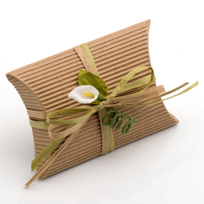 Op de afbeelding: Een bruine kartonnen kussenbox met een groen lint en een witte bloem. De doos is vastgebonden met een groen lint en heeft een witte bloem bovenop.