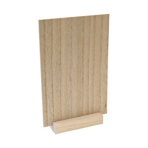 May include: A wooden sign holder with a light brown finish. The sign is rectangular and stands upright, supported by a small, rectangular wooden base. The wood grain is visible on both the sign and the base.