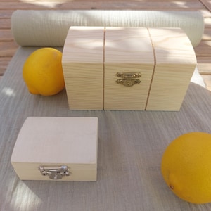May include: Two wooden boxes with latches, one larger than the other, on a light brown fabric surface. Two yellow lemons are also on the surface.
