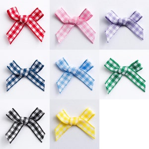 Könnte beinhalten: Neun Gingham-Schleifen in verschiedenen Farben, darunter Rot, Rosa, Lila, Blau, Grün, Gelb und Schwarz. Jede Schleife ist mit einem weißen Gingham-Muster gebunden.