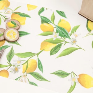 May include: A white table runner with a watercolour lemon design. The runner features yellow lemons, green leaves, and white blossoms. Wooden coasters with lemon slice designs are also visible.