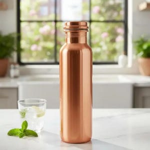 May include: A copper-colored water bottle with a cylindrical shape. The bottle is made of metal and has a screw-on cap. A glass of water with ice and mint sits next to the bottle on a white countertop.