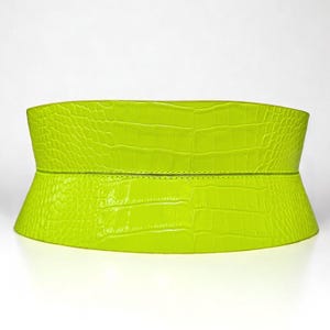 May include: A bright neon green wide belt with a crocodile texture. The belt is made of a single piece of material and has a slight curve to it. The belt is designed to be worn around the waist.