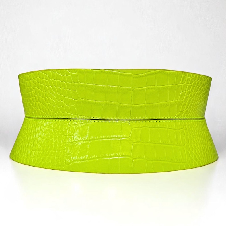 May include: A bright neon green wide belt with a crocodile texture. The belt is made of a single piece of material and has a slight curve to it. The belt is designed to be worn around the waist.