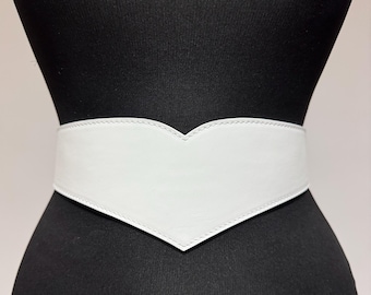 May include: A white leather belt with a heart-shaped design. The belt is wide and has a smooth finish.
