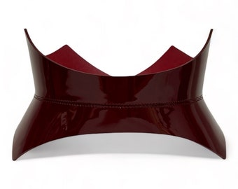 May include: A burgundy leather choker with a pointed, curved design. The choker has a glossy finish and a stitched seam around the edge.