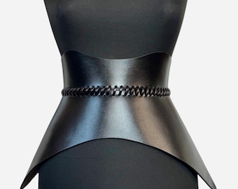 May include: A black leather corset with a chain detail. The corset is shaped like a heart and has a pointed bottom.