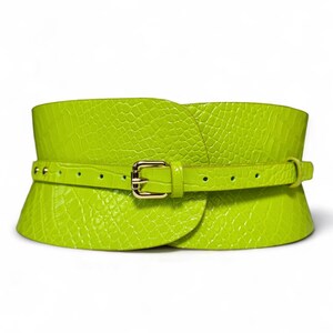 May include: A wide, lime green belt with a textured, crocodile-like pattern. The belt features a smaller, matching belt that fastens with a gold-colored buckle. The design is a wide corset style, with a wrap-around shape.