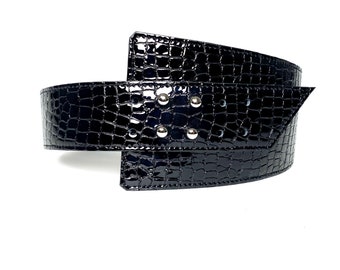 May include: A black, wide belt with a glossy, crocodile-skin texture. The belt features silver-colored rivets and a unique, overlapping design. The belt is approximately 3 inches wide.