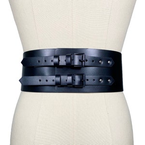 Könnte beinhalten: Ein breiter schwarzer Ledergürtel mit zwei Reihen doppelter Schnallen. Der Gürtel wird auf einem weißen Mannequin gezeigt.