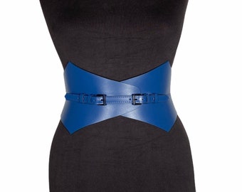 Pode incluir: Um cinto de couro azul com um design cruzado e fivelas duplas. O cinto é largo e tem uma forma pontiaguda.