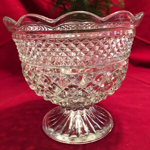 May include: A clear glass bowl with a scalloped rim and a diamond-shaped pattern. The bowl sits on a pedestal base with a fluted design.