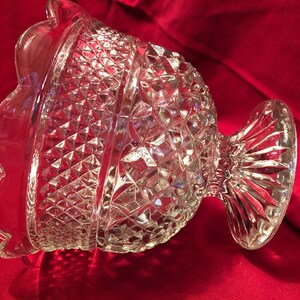 May include: A clear glass bowl with a scalloped edge and a diamond pattern. The bowl has a pedestal base.