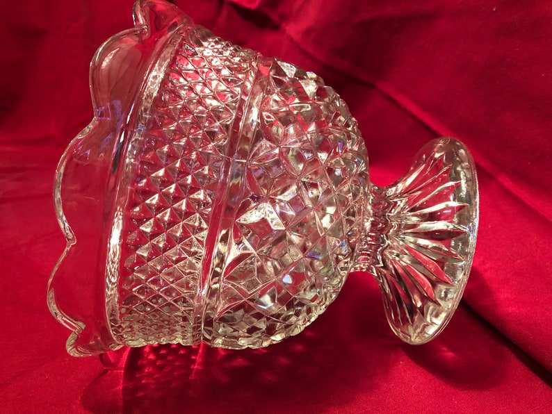 May include: A clear glass bowl with a scalloped edge and a diamond pattern. The bowl has a pedestal base.