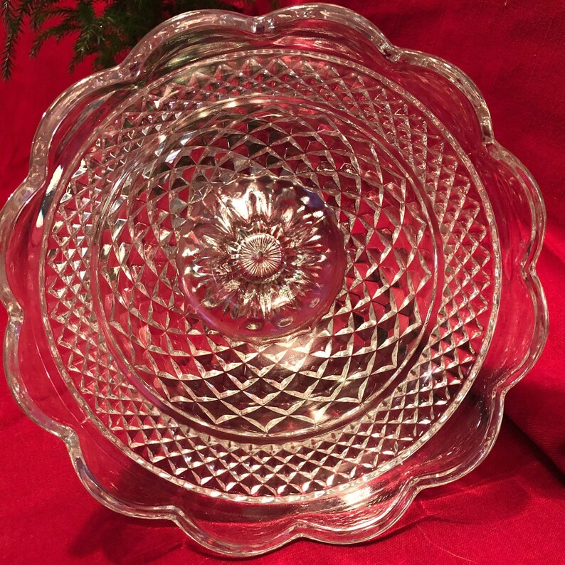 May include: A clear glass cake stand with a scalloped edge and a diamond pattern. The stand is designed for serving desserts or other treats.