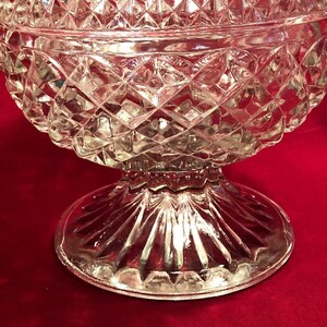 May include: A clear glass bowl with a diamond pattern and a fluted base. The bowl is on a red surface.