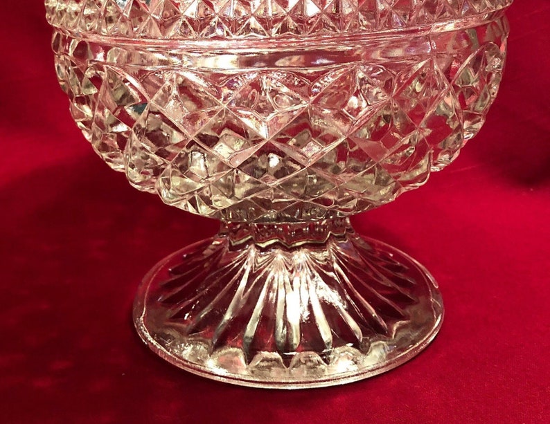 May include: A clear glass bowl with a diamond pattern and a fluted base. The bowl is on a red surface.