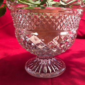 May include: A clear glass vase with a diamond pattern and a pedestal base. The vase is empty.