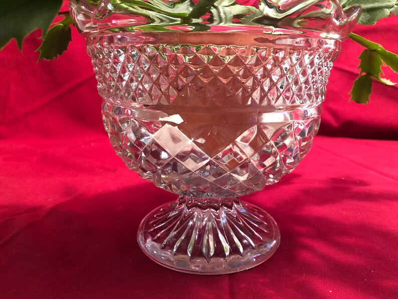 May include: A clear glass vase with a diamond pattern and a pedestal base. The vase is empty.