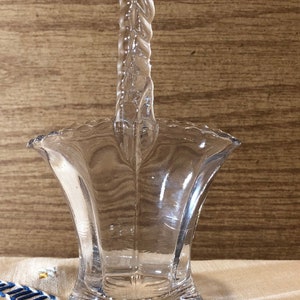 May include: A clear glass basket with a twisted handle. The basket has a scalloped rim and a fluted base.