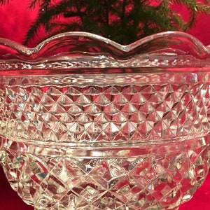 May include: A clear glass bowl with a scalloped rim and a diamond-shaped pattern. The bowl is made of thick glass and has a heavy base.