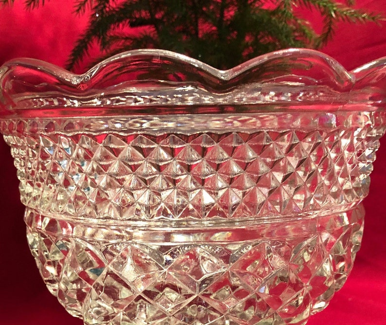 May include: A clear glass bowl with a scalloped rim and a diamond-shaped pattern. The bowl is made of thick glass and has a heavy base.