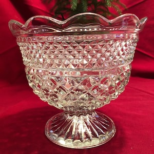 May include: A clear glass bowl with a scalloped rim and a diamond-shaped pattern. The bowl sits on a pedestal base.