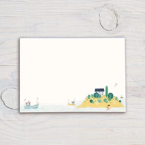 Puede incluir: Un bloc de notas rectangular con una ilustración en acuarela de una escena costera. La imagen presenta una pequeña isla con una casa, árboles y una persona surfeando. Dos barcos están en el agua. El bloc de notas está sobre una superficie de madera blanca.