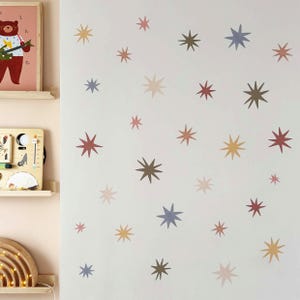 May include: A white wall decorated with star-shaped decals in shades of brown, yellow, red, and blue. The stars are of different sizes and are spread across the wall, creating a whimsical, celestial theme. The room has a playful, decorative aesthetic.