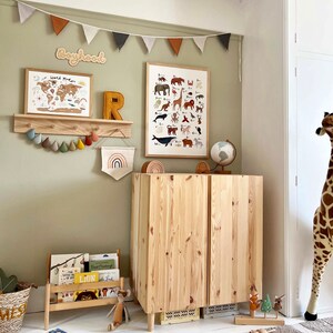 May include: A light green nursery with a wooden cabinet, a globe, a world map, and a wooden shelf with a wooden letter R and a banner of colorful felt teardrop shapes. The wall is decorated with a banner of colorful triangle flags and a wooden sign that says "Boyhood".