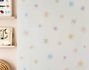May include: A white wall adorned with pastel-colored star decals. The stars are in shades of pink, yellow, green, and blue. The image also shows a wooden shelf with a framed color chart and a wooden toy.