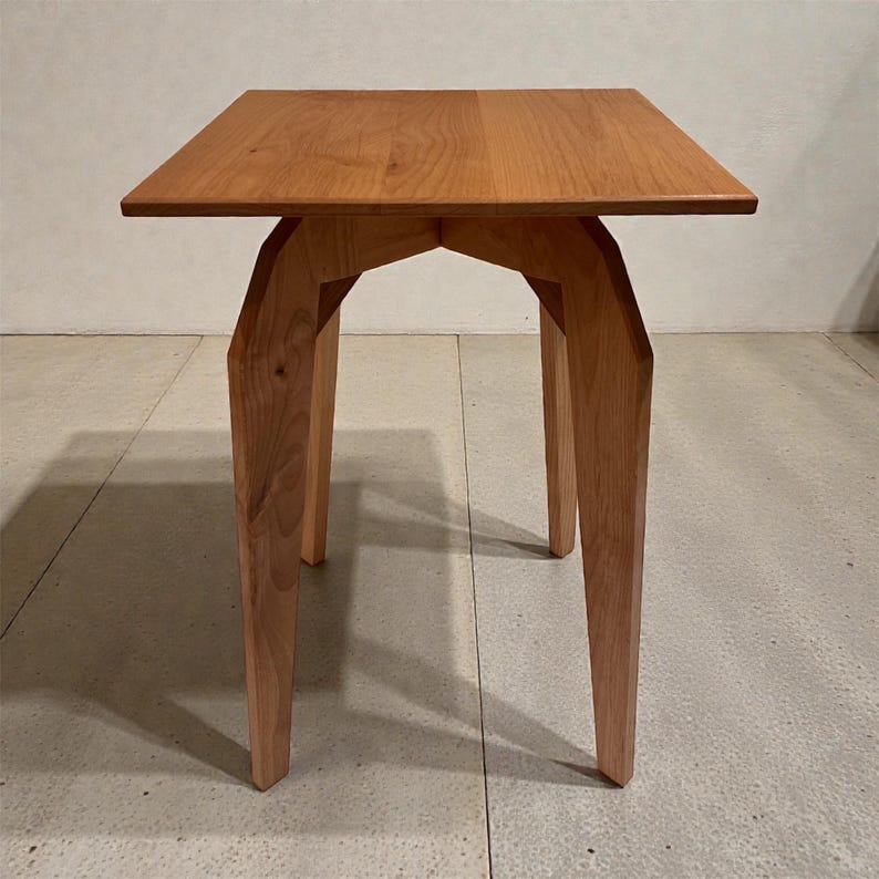 K&ouml;nnte beinhalten: Kleiner, quadratischer Beistelltisch aus Holz mit nat&uuml;rlicher Oberfl&auml;che. Die Tischplatte wird von vier abgewinkelten Beinen getragen, wodurch ein einzigartiges geometrisches Design entsteht. Der Tisch ist etwa 61 cm hoch.