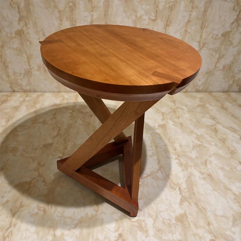 May include: A handcrafted wooden side table with a round top and a unique, angular base. The table is made of light and dark brown wood, with a smooth, polished finish. The table is approximately 20 inches tall.