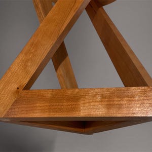 May include: A wooden geometric sculpture featuring intersecting triangular forms. The natural wood has a warm, reddish-brown hue. The design creates a three-dimensional effect, showcasing the craftsmanship and the interplay of angles and planes.
