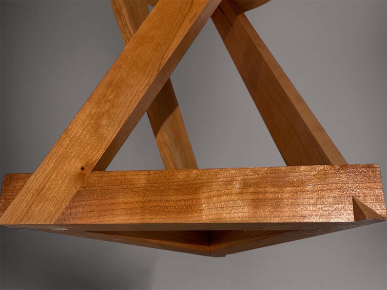 May include: A wooden geometric sculpture featuring intersecting triangular forms. The natural wood has a warm, reddish-brown hue. The design creates a three-dimensional effect, showcasing the craftsmanship and the interplay of angles and planes.