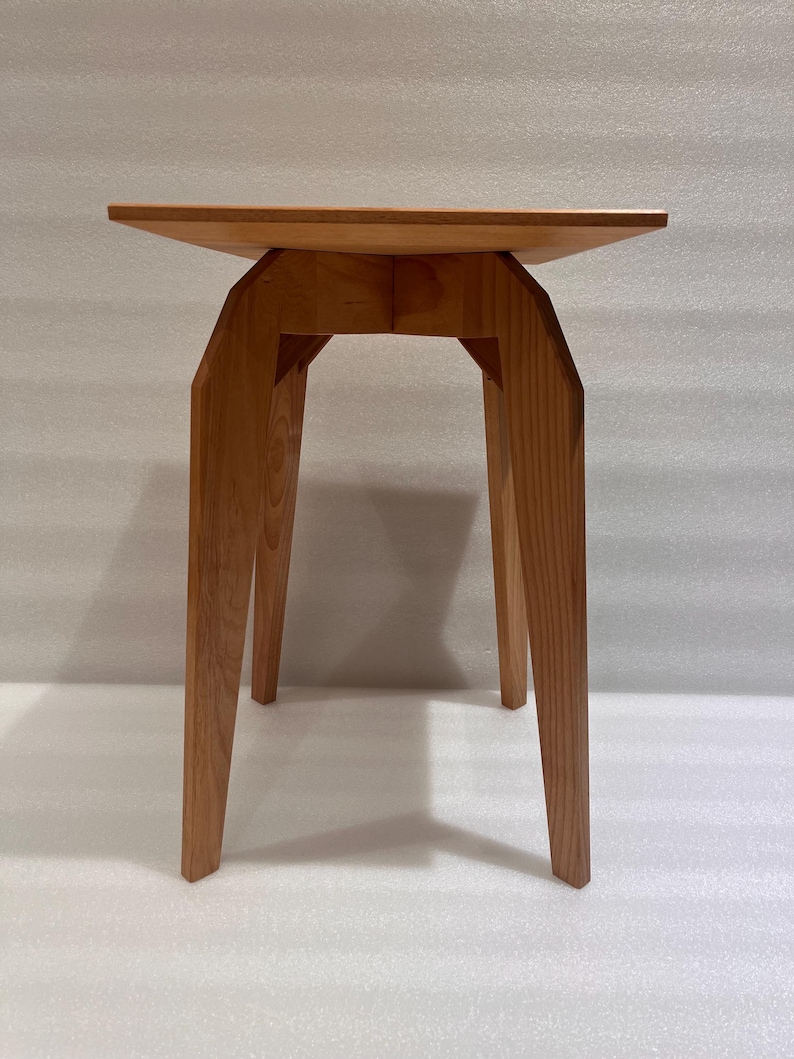 K&ouml;nnte beinhalten: Ein hellbrauner Beistelltisch aus Holz mit quadratischer Oberseite und abgewinkelten Beinen. Der Tisch ist aus Massivholz gefertigt und hat eine nat&uuml;rliche Oberfl&auml;che. Die Beine sind geometrisch geformt und verleihen einen modernen Touch. Der Tisch ist ca. 61 cm hoch.