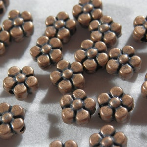 May include: A collection of copper-colored metal flower-shaped beads. The beads have five petals and a small hole in the center.